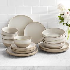 a table topped with white plates and bowls next to a vase filled with flowers on top of a counter