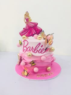 a pink cake with barbie on top and gold decorations around it's edges, sitting on a white surface