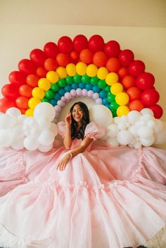 a woman laying on top of a bed under a rainbow shaped balloon wall with balloons