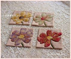 four embroidered coasters sitting on top of a lace covered tablecloth with flowers in the center