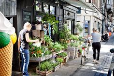 an ice cream shop with plants and people walking down the street