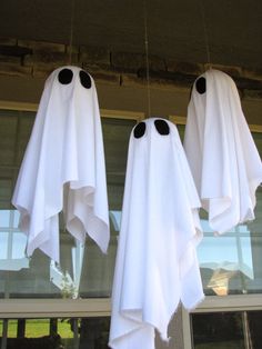 three white ghost decorations hanging from the ceiling in front of a window with two black eyes on them