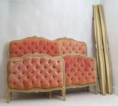 an old fashioned bed with pink velvet upholstered and gold trimmings, against a white wall