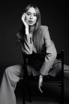 a woman sitting in a chair with her hand on her head and looking at the camera