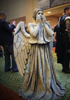 a statue of an angel is standing in the middle of a room with other people