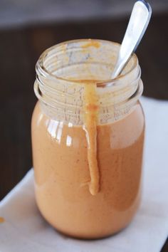 a glass jar filled with caramel sauce on top of a white tablecloth next to a spoon