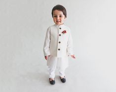 a young boy wearing a white outfit and black shoes standing in front of a white wall