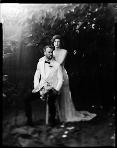 an old black and white photo of a man in a tuxedo standing next to a woman