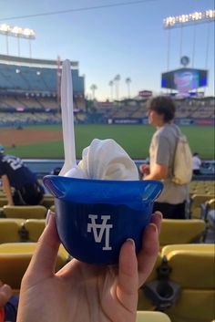 a person holding up a blue bowl filled with ice cream at a baseball game in the sun