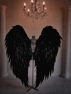 a mannequin with black angel wings on it's head and chandelier in the background