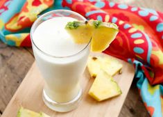 a glass filled with milk next to sliced pineapples on a wooden cutting board