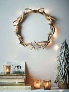 a wreath made out of antlers on top of a mantle next to candles and a christmas tree