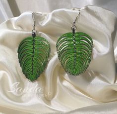 a pair of green leaf shaped earrings sitting on top of a white cloth covered table