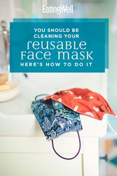 a cloth face mask sitting on top of a white counter next to a blue sign that says, you should be cleaning your reusable face mask here's how to do it