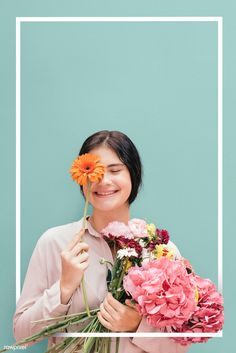 a woman holding flowers in her hands and smiling at the camera, against a blue background