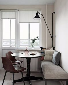 a table with two chairs and a bench in front of the window, next to a wall mounted lamp