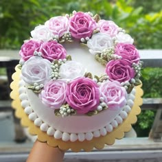 a hand holding a cake with pink and white flowers on it