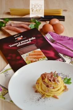 a white plate topped with spaghetti next to eggs and meat on top of a wooden table