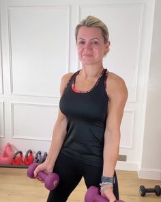 a woman holding two purple dumbs while standing in front of a gym equipment rack