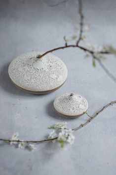 two small white vases sitting next to each other on a gray surface with flowers