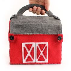 a hand holding a red and grey felt bag with two white squares on the front