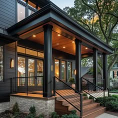 a modern house with wooden steps and black railings on the front porch, surrounded by trees