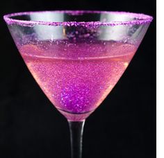 a purple drink in a wine glass on a black background with pink flecks