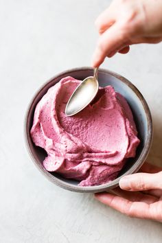 a person holding a spoon over a bowl of pink ice cream