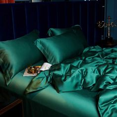 a bed with green sheets and pillows in a dark blue room, next to a night stand