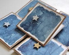 three cards with gold stars on them and blue watercolor paper in the back ground