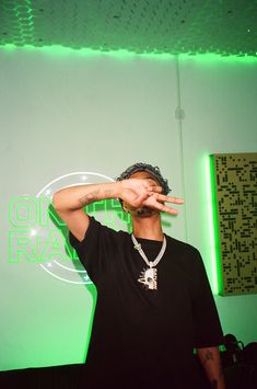 a man making the peace sign with his hand while standing in front of a green wall