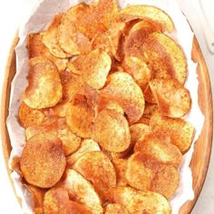 a wooden bowl filled with fried potatoes on top of a white tablecloth and utensils