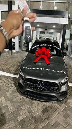 a person holding a cell phone in front of a car with a red bow on it