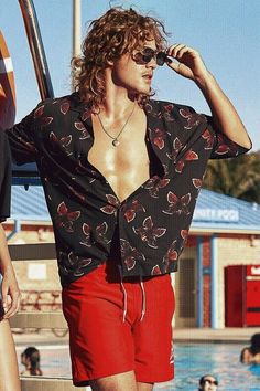 a man in red shorts and a black shirt standing next to a swimming pool