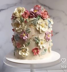 a white cake with flowers on it sitting on a stand in front of a marble wall