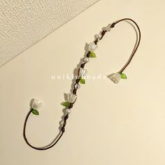 the necklace is decorated with white flowers and green leaves on brown leather cord for decoration