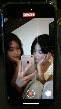 two women looking at an iphone screen with the same image on it as they look at each other