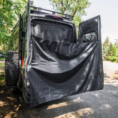 the back end of an off road vehicle covered with a black tarp and some trees in the background