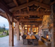 an outdoor dining area with stone fireplace and wood beams, surrounded by large wooden pillars