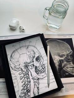 an open book with a drawing of a human skull on it next to earbuds and headphones