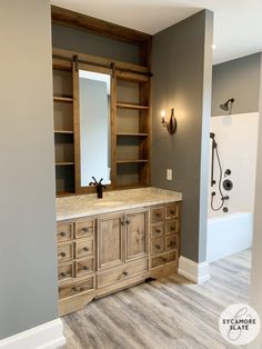 a bathroom with gray walls and wooden cabinetry in the middle, along with a large mirror