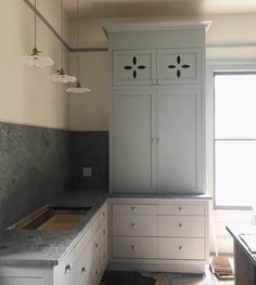 an empty kitchen with white cabinets and gray counter tops in front of a large window