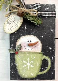 a christmas card with a snowman in a green cup on the front and an ornament attached to it