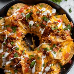 a skillet filled with nachos covered in cheese and toppings, ready to be eaten