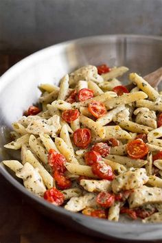 a bowl filled with pasta and tomatoes on top of a wooden table