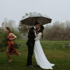 a bride and groom kissing under an umbrella in the rain while two other people run behind them