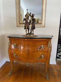 an antique dresser with two figurines on top and a mirror in the background