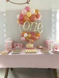 a table topped with cake and balloons next to a sign that says one on it