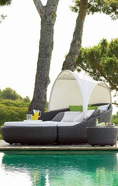 an outdoor lounge chair sitting next to a swimming pool with trees in the back ground