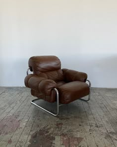 a brown leather recliner chair sitting on top of a hard wood floor next to a white wall